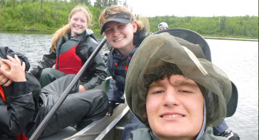 Three people sitting in canoes smile for the photo